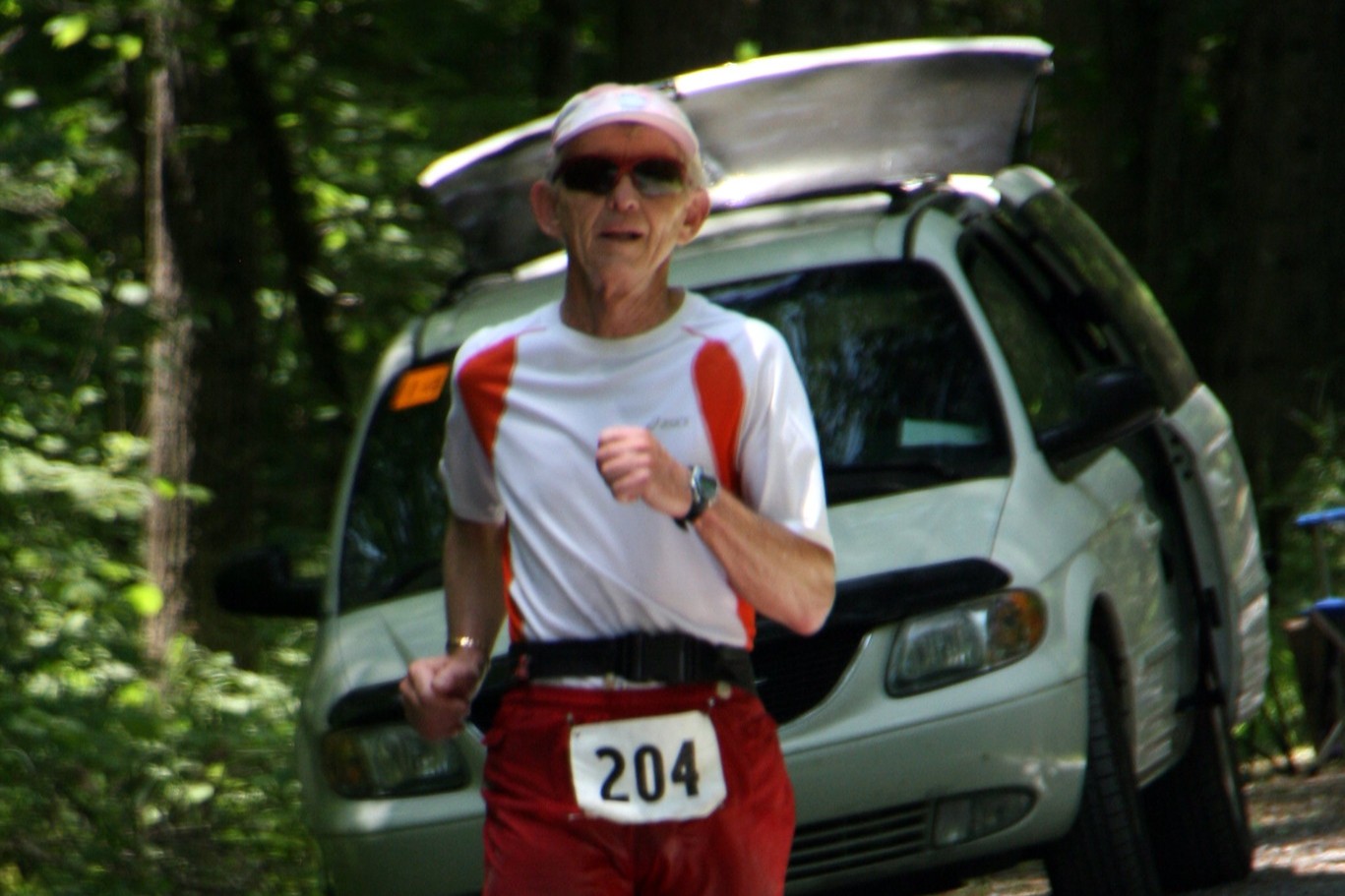 Group of 4 runners all in white shirts walking on gravel road with their back to the camera.
