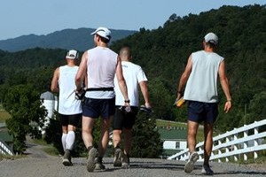 Group of 4 runners all in white shirts walking on gravel road with their back to the camera.