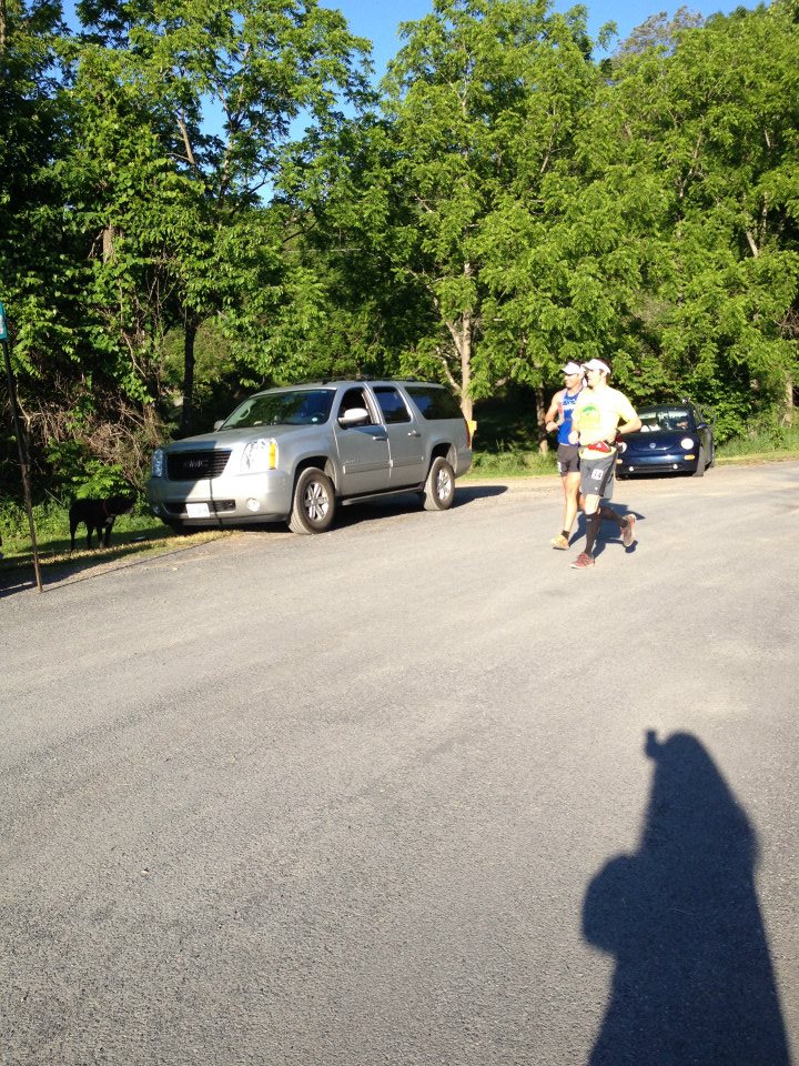 2 runners on the road. 2 cars parked in the background