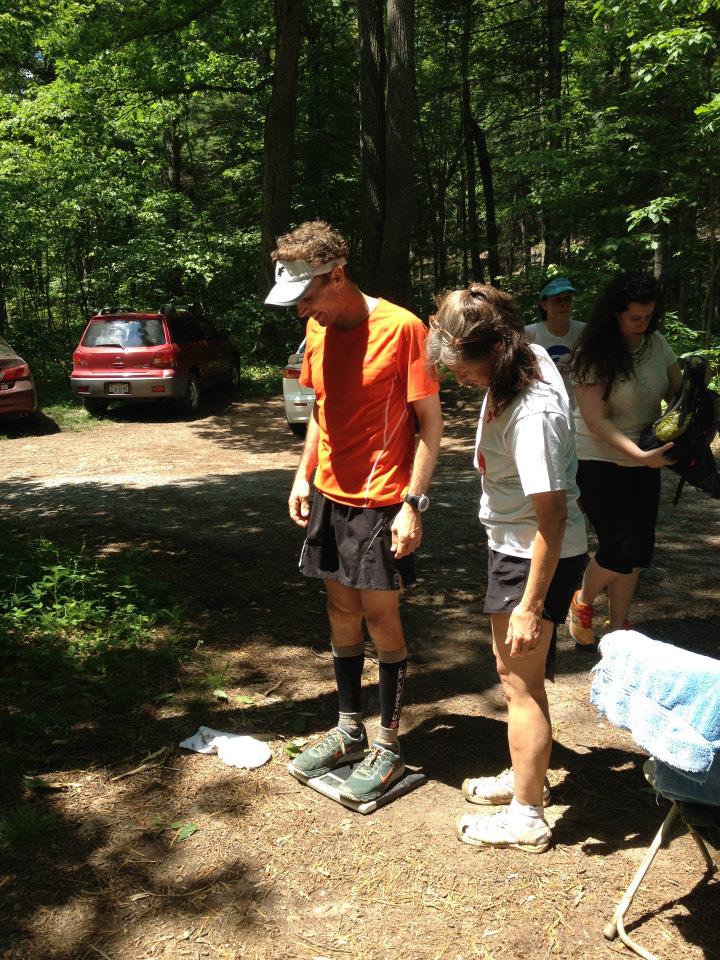 Runner in orange shirt stands on scale, while women in white shirt looks at scale