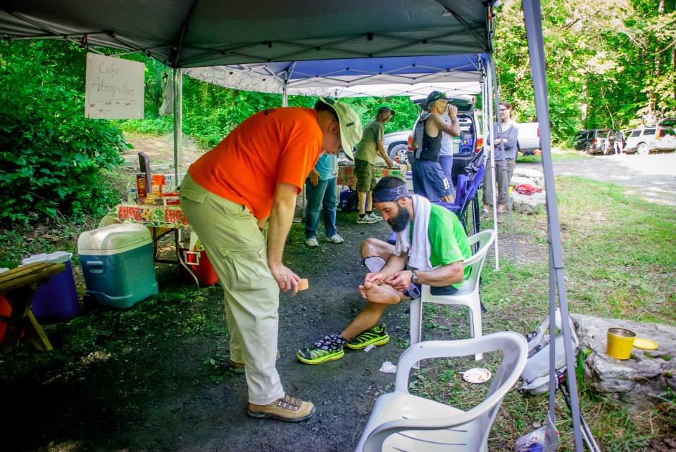 Runner sits in a chair to adjust their shoe at an aid station