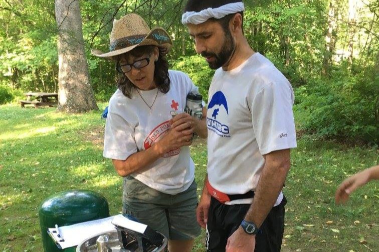 Runner in white shirt stands on scale, while medical team member looks at the numbers