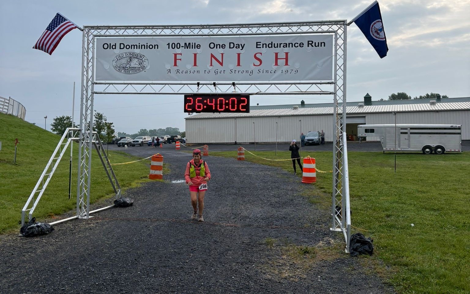 Female runner
            crosses under finish line. Clock shows 26:40:02