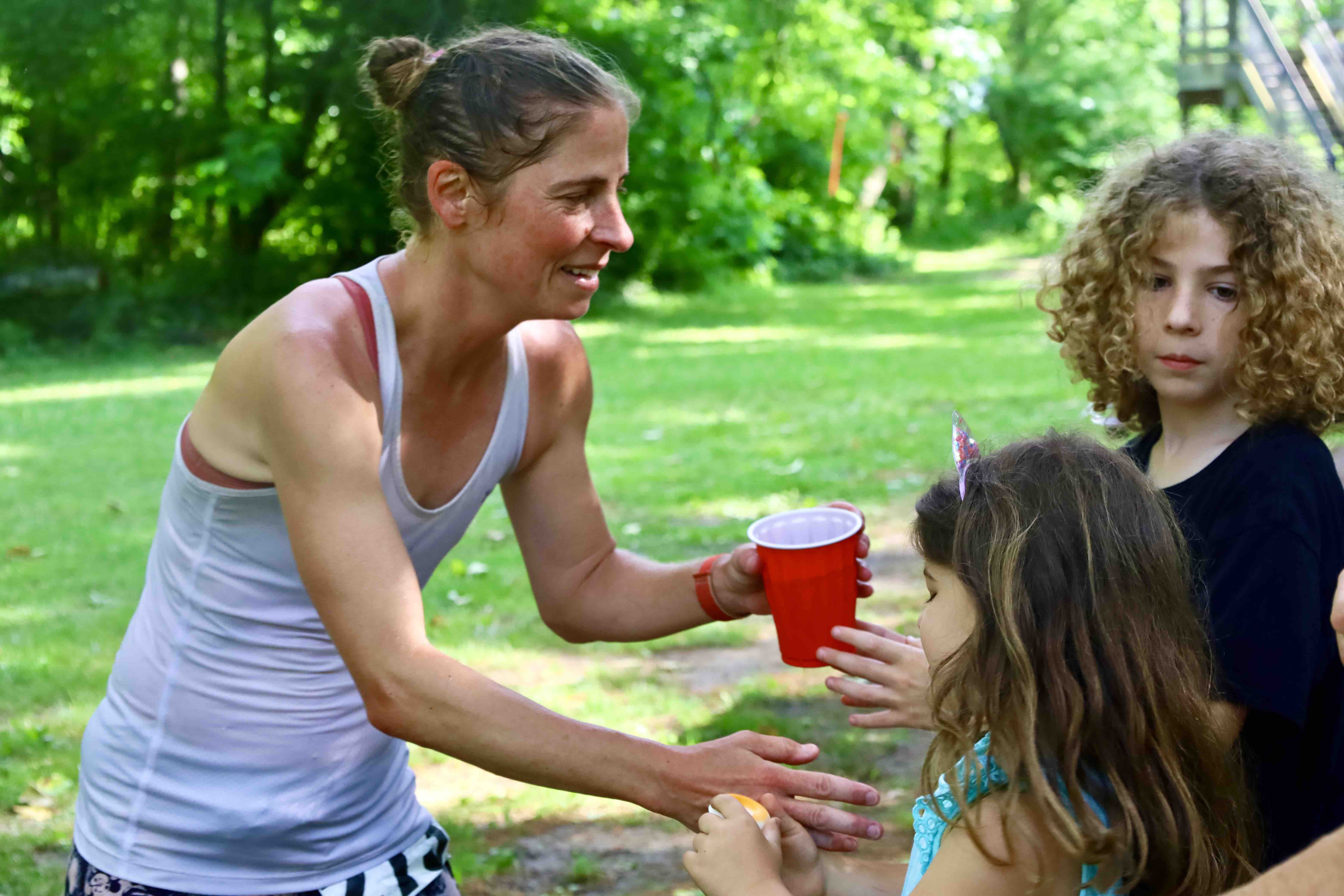 Runner in white tank top takes a red cup at an aid station