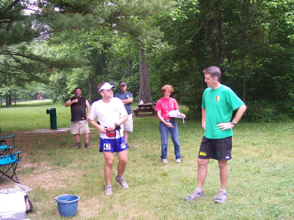 Runner in white visor talking with a crew member in green shirt. People walking behind